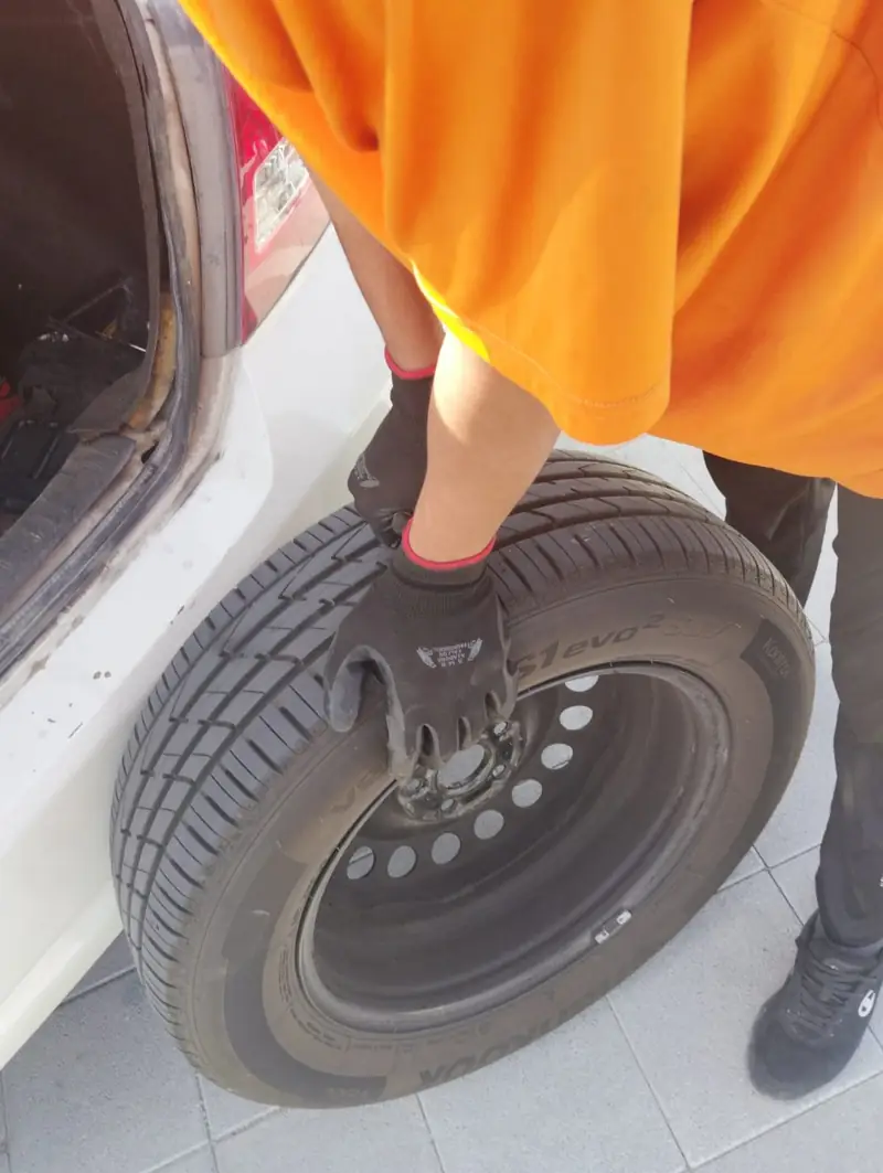 Technician carrying a wheel to a car